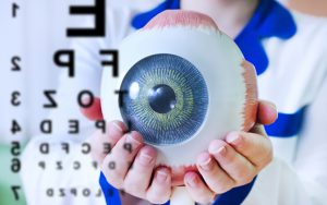 A person holding an eye with an eye chart in the background.